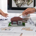 A professional team at a Renovation Company Dubai reviewing a miniature house model and floor plans on a desk to plan a home remodeling project.
