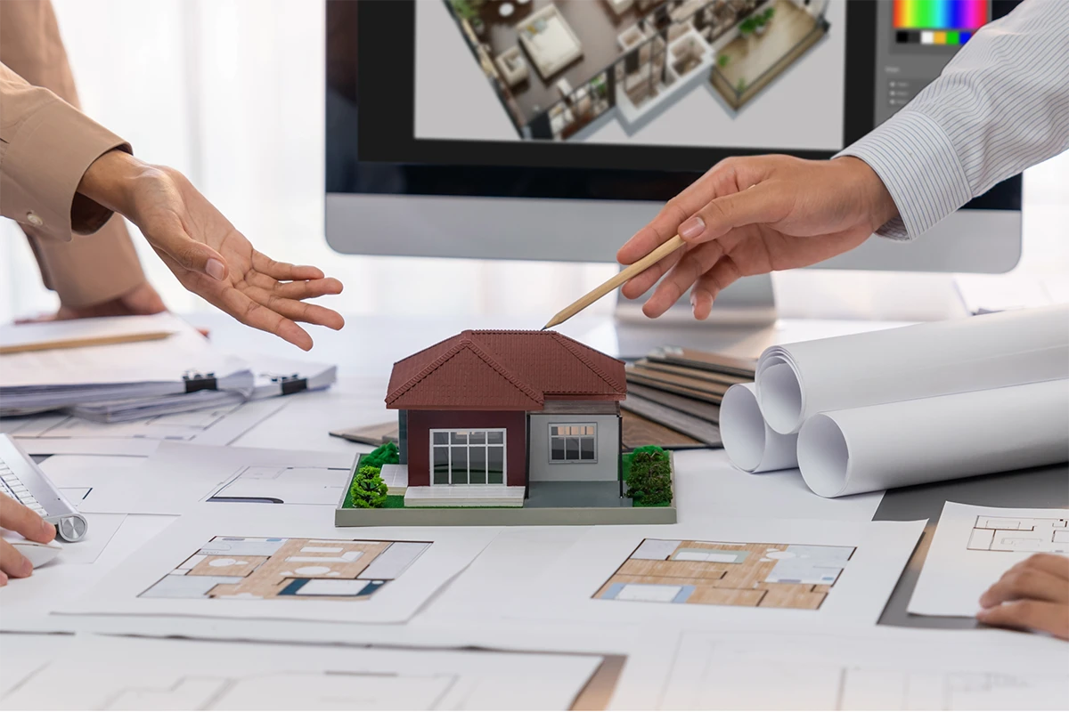 A professional team at a Renovation Company Dubai reviewing a miniature house model and floor plans on a desk to plan a home remodeling project.