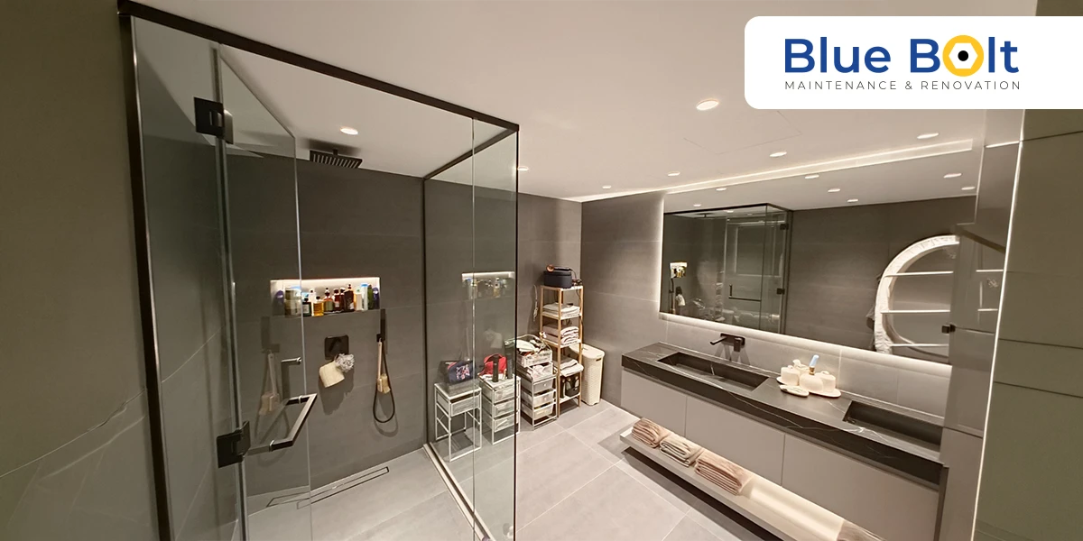 A modern bathroom remodeling Dubai project featuring a walk-in glass rain shower, charcoal grey wall tiles, and a floating double vanity with integrated lighting.