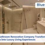 A modern, bathroom designed by a Bathroom renovation company, featuring a dual-sink vanity, glass-enclosed walk-in shower with rainfall heads, and warm ambient lighting.